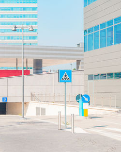 Road sign by building against clear blue sky