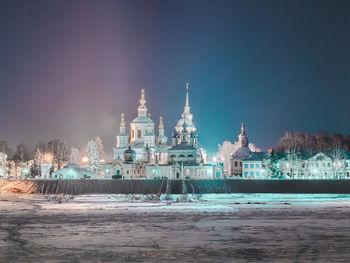 Illuminated buildings by sea against sky at night