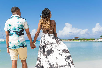 Rear view of a young couple holding hands and standing at the beach while looking toward the horizon