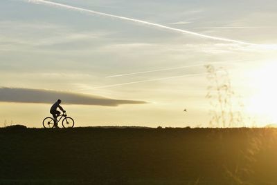 Silhouette man riding bicycle on field against sky