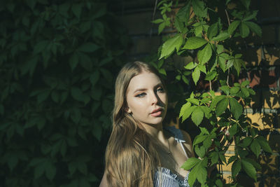 Thoughtful beautiful young woman standing by plants in park