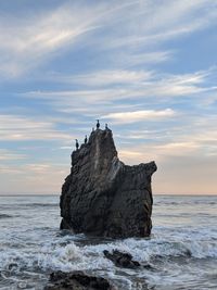 Rock formation on beach against sky during sunset