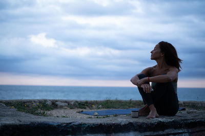 Side view of woman sitting relaxed after doing a yoga session in a natural environment by the sea.