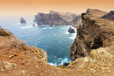 High angle view of rocky coastal feature against clouds