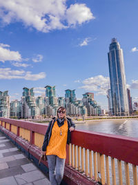 Portrait of smiling man standing by railing against buildings in city