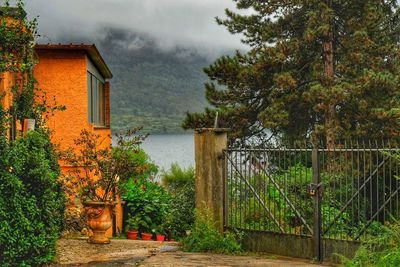 House by lake amidst trees and building against sky