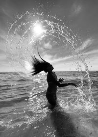 Girl with wet tousled hair standing in sea against sky