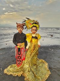 Portrait of girl and boy in traditional clothes standing at beach against sky