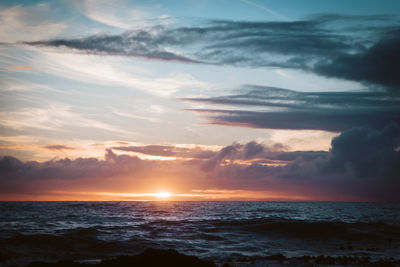 Scenic view of sea against cloudy sky during sunset