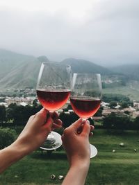 Two glasses of rose wine in two hands in fronf of mountains