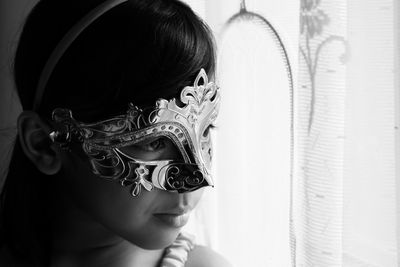 Close-up of thoughtful girl wearing mask while looking through window at home