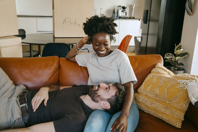 Smiling man lying down on girlfriend's lap sitting on sofa at new home