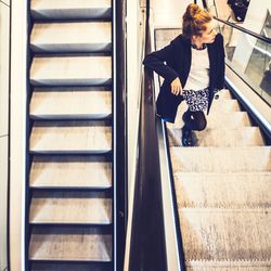 High angle view of woman standing on escalator at shopping mall