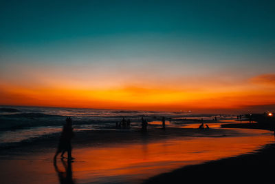 Silhouette people on beach against sky during sunset