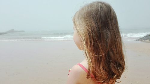 Rear view of woman standing on beach against sky