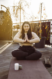 Woman doing yoga while sitting with hands clasped on exercise mat at terrace