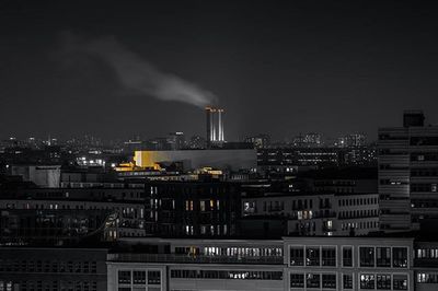 Smoke emitting from illuminated city against sky at night