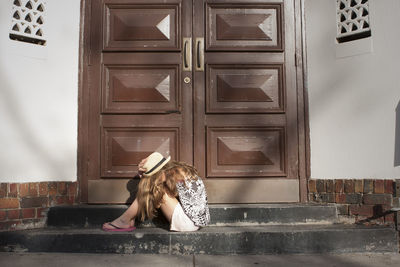 Full length of young woman sitting against closed doors