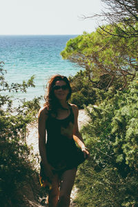 Portrait of young woman standing by sea against sky