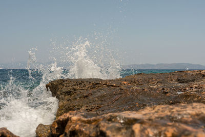 Waves splashing on rocks at shore against sky