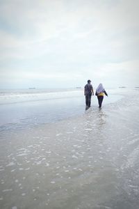 Rear view of people on beach against sky