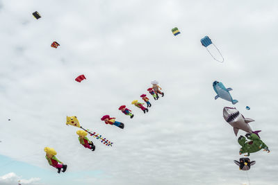 Low angle view of various colorful balloons flying against cloudy sky