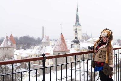 Woman holding camera while standing by railing at observation point during winter