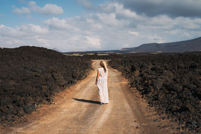 Rear view of woman standing on dirt road against sky