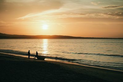 Silhouette man in sea against sky during sunset