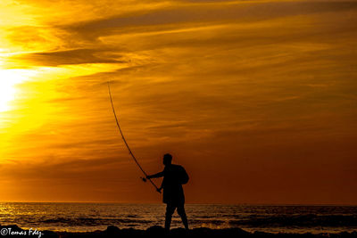 Silhouette man on beach against sky during sunset