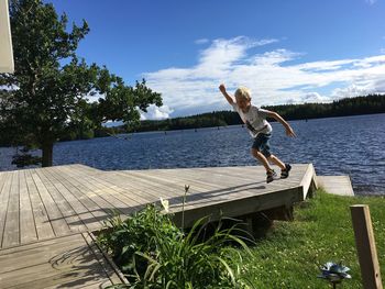 Full length of boy running on pier over lake against blue sky during sunny day