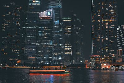 Illuminated buildings by river in city at night