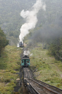 Two steam locomotives of mount washington cog railway pushing coaches to the summit at good weather.