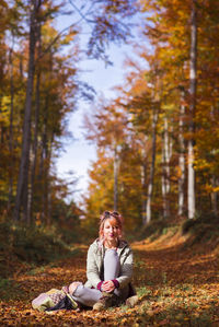 Portrait of young woman sitting on field in forest during autumn