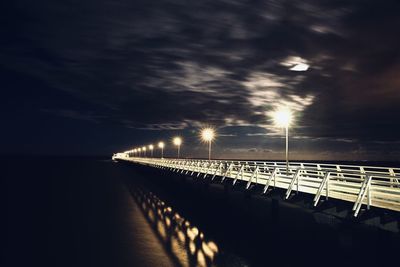 Illuminated bridge over sea against sky at night