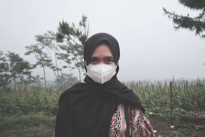 Portrait of young woman make a mask standing on field against sky