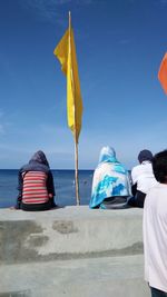 Rear view of people by flag on promenade against sky