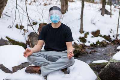 Portrait of man wearing masks sitting on rock by river