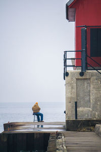 Full length rear view of man sitting on chair at pier