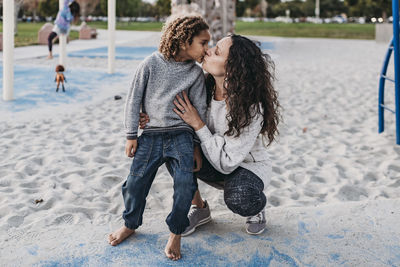 Mother giving son a kiss while playing on playground at dusk