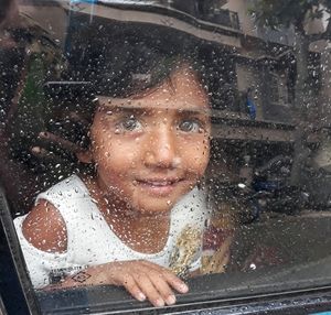 Portrait of happy girl looking through wet window