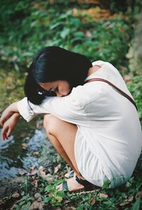 Side view of woman crouching on land in forest