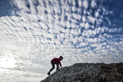 Side view of boy climbing mountain against cloudy sky