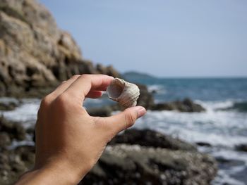 Close-up of hand holding rock at beach against clear sky