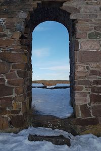 Stone wall by frozen window against sky