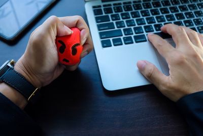 Cropped hand of businessman pressing stress ball while using laptop on table