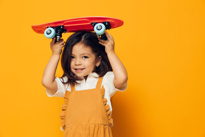 Portrait of young woman with arms raised standing against yellow background