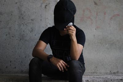 Man wearing cap while sitting against wall