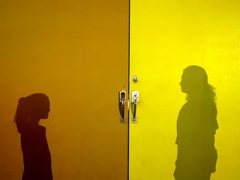 Side view of silhouette people standing against yellow wall