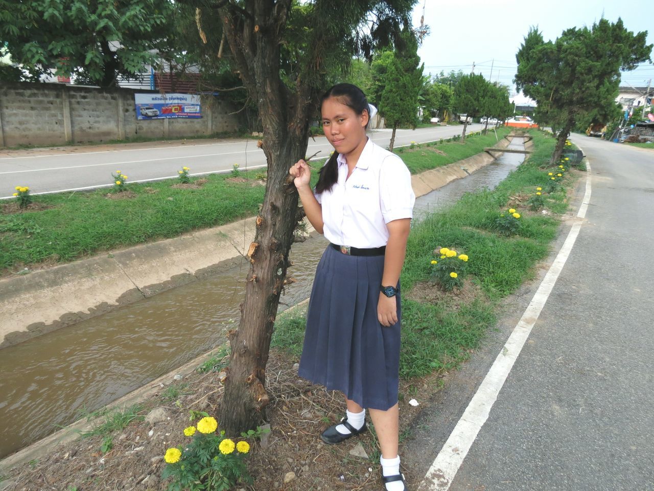 PORTRAIT OF SMILING YOUNG WOMAN STANDING BY TREE